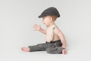 Cute baby boy sitting up wearing a flat cap in Sussex