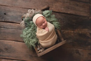 newborn baby photographs Sussex sleeping girl knitted bonnet pale yellow green curly layer wood background studio portraits by Samphire Photography