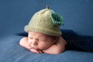 Experienced newborn photographer West Sussex sleeping baby boy knitted apple hat blue studio portrait Samphire Photography