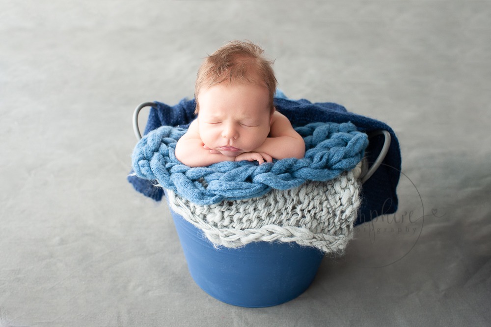 Experienced newborn photographer West Sussex sleeping baby boy blue knit layers bucket studio portrait Samphire Photography