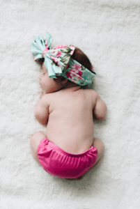 baby wearing floral headband and pink nappy cover