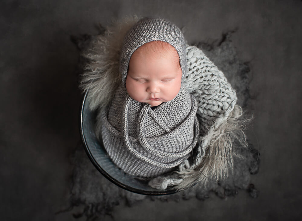 Choosing a newborn photographer showing a little boy in grey in a bucket