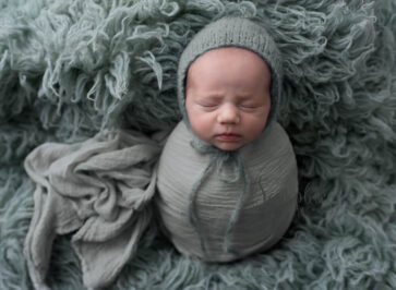 Newborn baby wrapped up in green swaddle