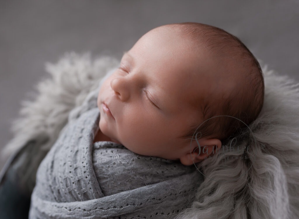 sleeping newborn baby boy swaddled in grey