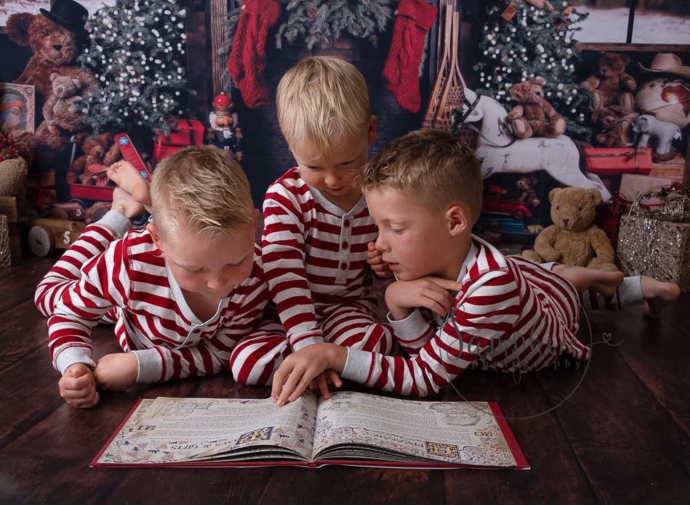 Christmas scene of young brothers wearing pyjamas reading book in front of fireplace
